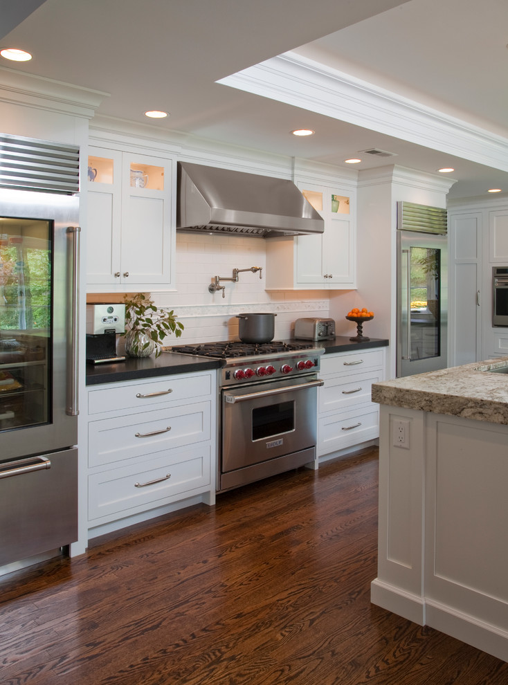This is an example of a traditional eat-in kitchen in Philadelphia with a farmhouse sink, flat-panel cabinets, white cabinets, granite benchtops, white splashback and stainless steel appliances.