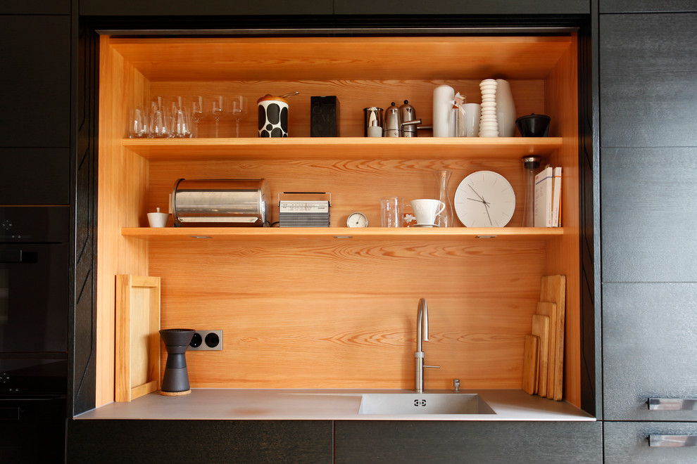 This is an example of a mid-sized contemporary galley eat-in kitchen in Nuremberg with an integrated sink, flat-panel cabinets, dark wood cabinets, concrete benchtops, black appliances, light hardwood floors, with island, timber splashback and grey benchtop.