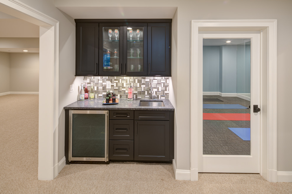 This is an example of a mid-sized transitional single-wall wet bar in DC Metro with an undermount sink, recessed-panel cabinets, dark wood cabinets, granite benchtops, multi-coloured splashback, mosaic tile splashback, carpet, beige floor and grey benchtop.