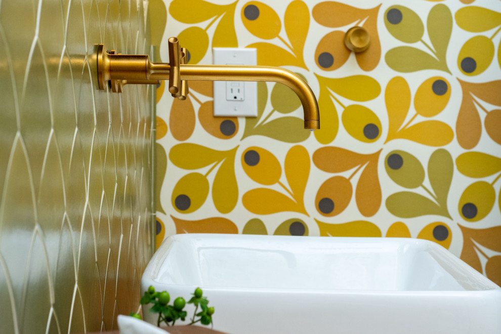 Inspiration for a mid-sized midcentury bathroom in Detroit with furniture-like cabinets, brown cabinets, a one-piece toilet, green tile, ceramic tile, multi-coloured walls, light hardwood floors, a vessel sink, wood benchtops, brown floor, brown benchtops, a freestanding vanity, vaulted and wallpaper.