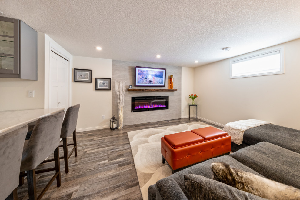 Inspiration for a mid-sized modern fully buried basement in Edmonton with a home bar, white walls, vinyl floors, a standard fireplace, a tile fireplace surround, brown floor and planked wall panelling.