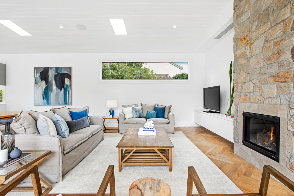 This is an example of a beach style open concept living room in Melbourne with white walls, medium hardwood floors, a standard fireplace, a freestanding tv, brown floor and timber.
