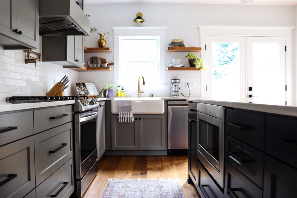 Design ideas for a mid-sized arts and crafts l-shaped eat-in kitchen in Miami with a farmhouse sink, shaker cabinets, grey cabinets, quartz benchtops, white splashback, porcelain splashback, stainless steel appliances, light hardwood floors, with island, brown floor and white benchtop.