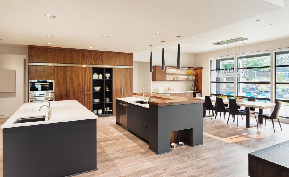 This is an example of an expansive midcentury single-wall eat-in kitchen in Los Angeles with an undermount sink, flat-panel cabinets, medium wood cabinets, quartz benchtops, white splashback, porcelain splashback, stainless steel appliances, light hardwood floors and multiple islands.
