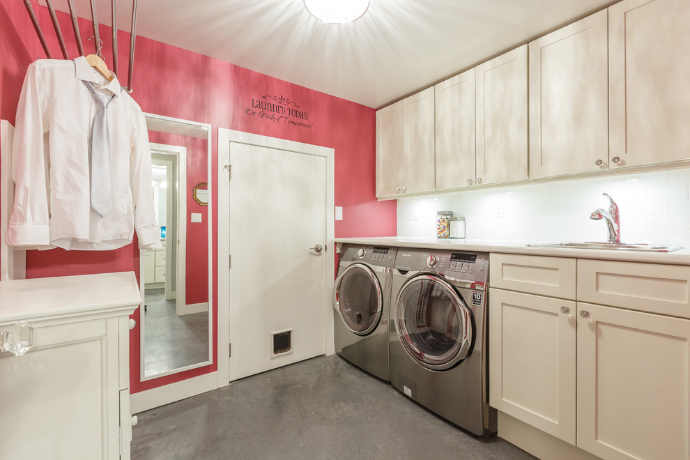 Mid-sized contemporary galley dedicated laundry room in Vancouver with a drop-in sink, shaker cabinets, white cabinets, laminate benchtops, pink walls, concrete floors and a side-by-side washer and dryer.