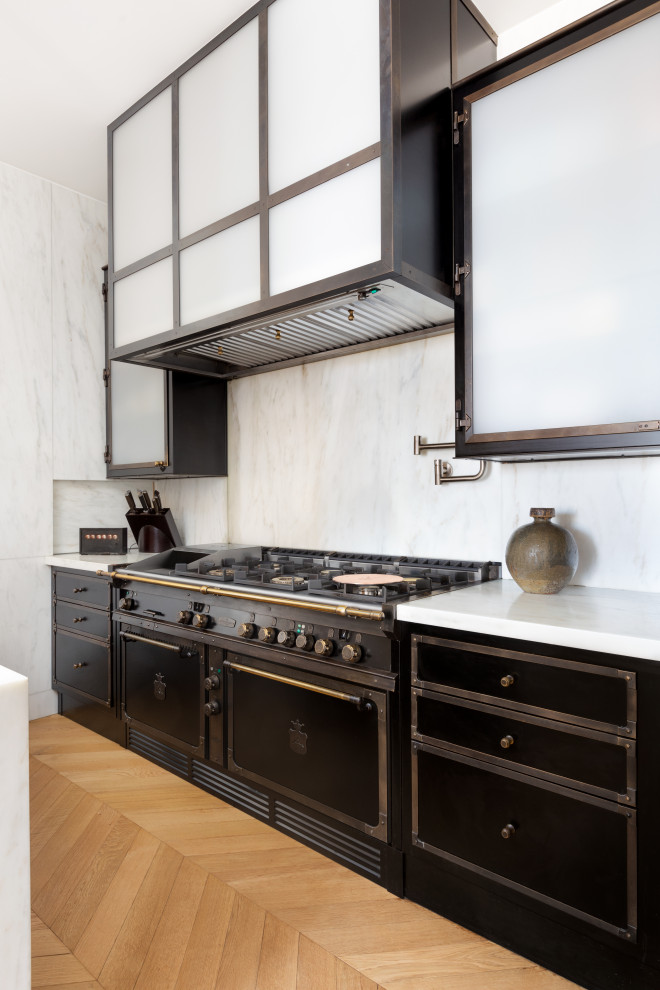 Mid-sized eclectic galley light wood floor and brown floor open concept kitchen photo in New York with an integrated sink, light wood cabinets, marble countertops, white backsplash, marble backsplash, black appliances, an island and white countertops