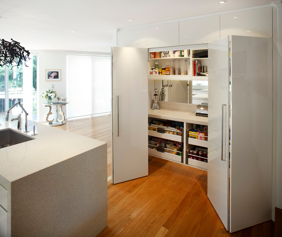Small contemporary galley kitchen in Sydney with an undermount sink, flat-panel cabinets, white cabinets, quartzite benchtops, white splashback, glass sheet splashback, stainless steel appliances, medium hardwood floors and with island.
