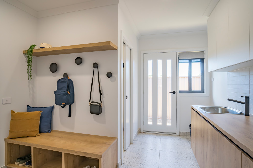 Large l-shaped utility room in Other with a drop-in sink, flat-panel cabinets, medium wood cabinets, laminate benchtops, white splashback, ceramic splashback, white walls, ceramic floors, a stacked washer and dryer, white floor and brown benchtop.