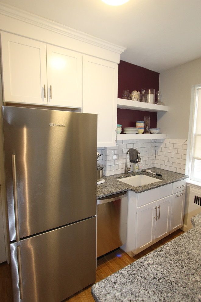 Photo of a small transitional galley separate kitchen in Boston with an undermount sink, flat-panel cabinets, white cabinets, granite benchtops, white splashback, ceramic splashback, stainless steel appliances, light hardwood floors, a peninsula and brown floor.