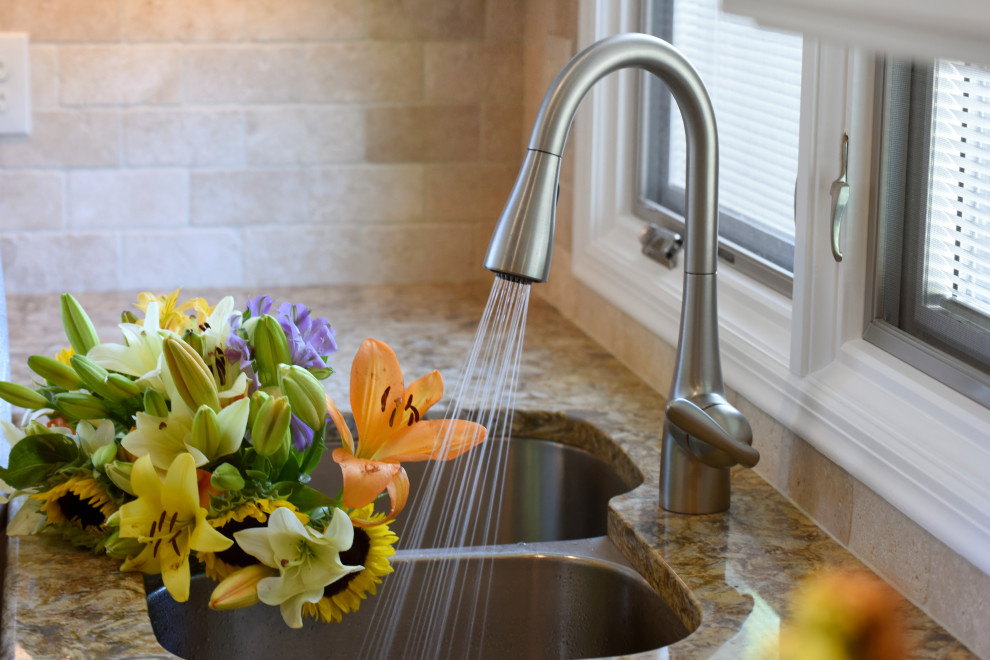 Inspiration for a mid-sized transitional u-shaped porcelain tile, beige floor and tray ceiling enclosed kitchen remodel with an undermount sink, flat-panel cabinets, beige cabinets, quartz countertops, beige backsplash, travertine backsplash, black appliances, an island and beige countertops
