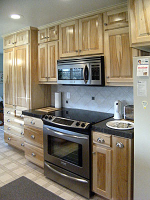 Example of a galley white floor kitchen design with raised-panel cabinets, stainless steel appliances, a peninsula and gray countertops