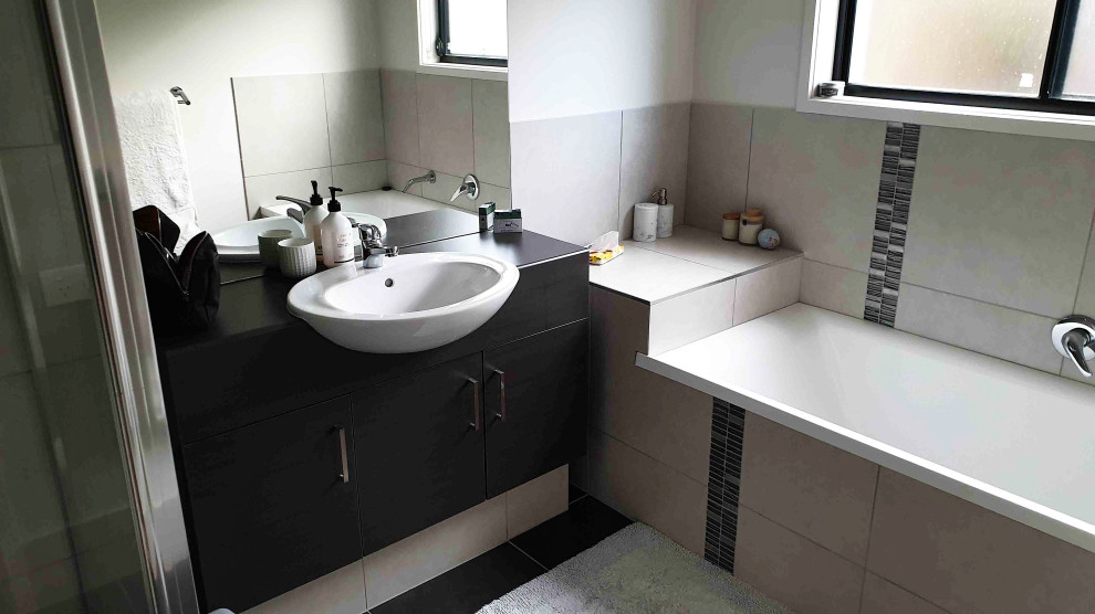 This is an example of a mid-sized contemporary bathroom in Sunshine Coast with black cabinets, beige tile, porcelain tile, white walls, porcelain floors, a drop-in sink, black floor and black benchtops.