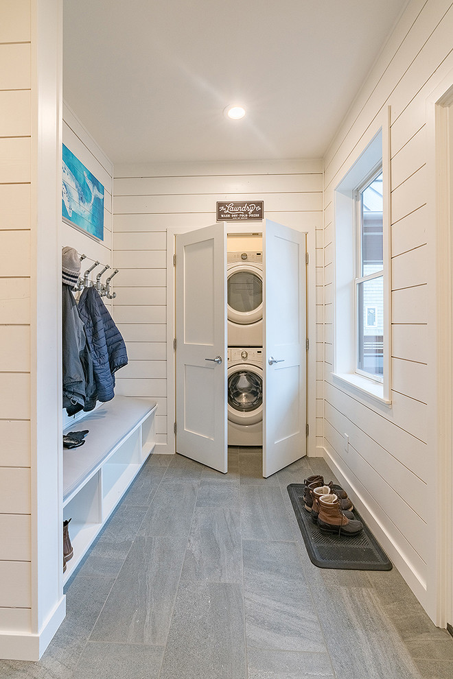This is an example of a mid-sized beach style laundry cupboard in Seattle with white walls, porcelain floors, grey floor and a stacked washer and dryer.