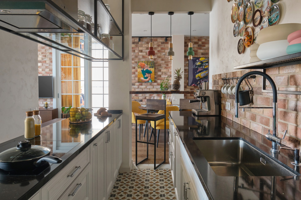 Industriell inredning av ett mellanstort brun brunt kök, med en enkel diskho, luckor med upphöjd panel, gröna skåp, bänkskiva i kvarts, brunt stänkskydd, stänkskydd i tegel, svarta vitvaror, klinkergolv i keramik, en köksö och orange golv