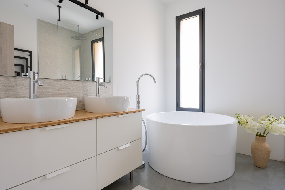 Modern inredning av ett stort vit vitt badrum med dusch, med luckor med profilerade fronter, ett fristående badkar, en kantlös dusch, en vägghängd toalettstol, vit kakel, keramikplattor, vita väggar, betonggolv, ett nedsänkt handfat, träbänkskiva, grått golv och med dusch som är öppen