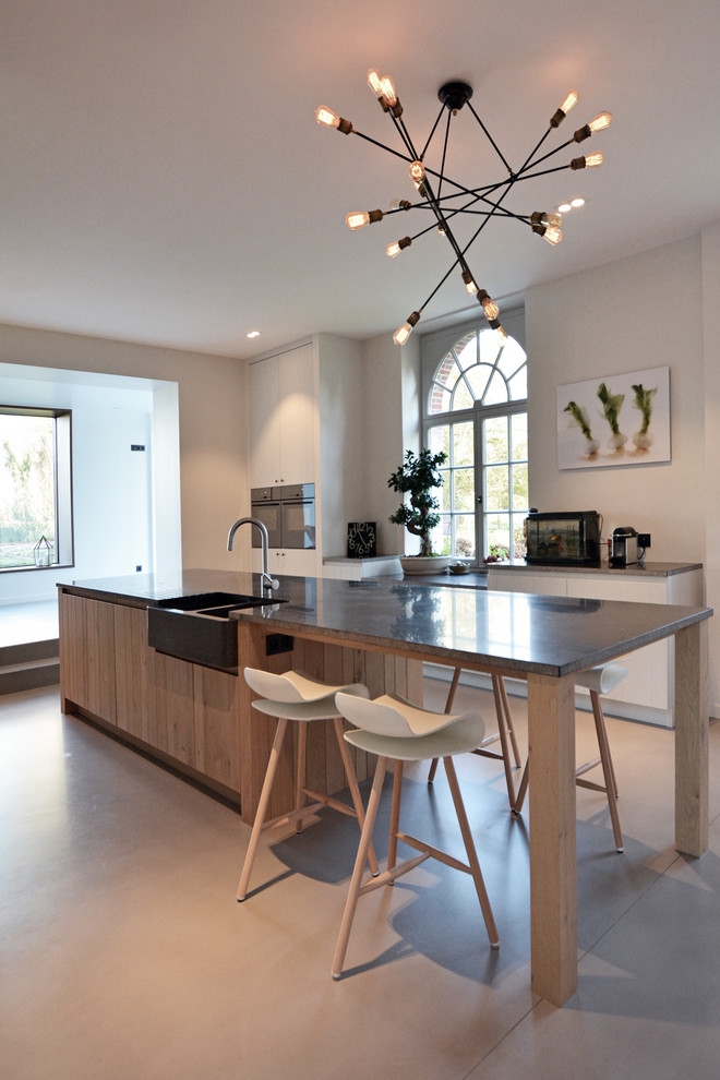 Inspiration for a large contemporary galley eat-in kitchen in Paris with a farmhouse sink, with island, panelled appliances, beaded inset cabinets, light wood cabinets, granite benchtops, black splashback, terra-cotta splashback and concrete floors.