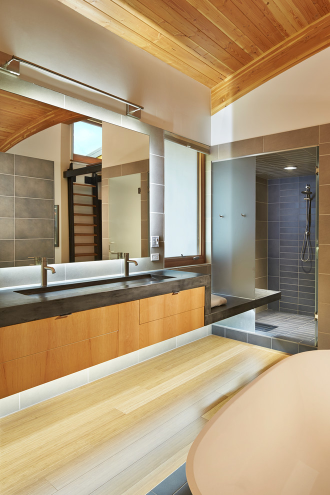 Design ideas for a contemporary master bathroom in Seattle with flat-panel cabinets, medium wood cabinets, gray tile, a trough sink, an alcove shower, white walls, light hardwood floors and concrete benchtops.
