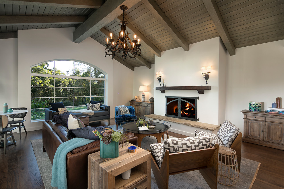 Inspiration for a large mediterranean living room in Santa Barbara with white walls, dark hardwood floors, a standard fireplace, a plaster fireplace surround and brown floor.