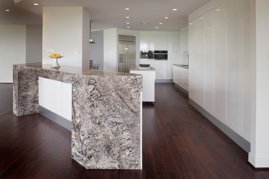 Mid-sized minimalist galley medium tone wood floor eat-in kitchen photo in Houston with an undermount sink, flat-panel cabinets, white cabinets, solid surface countertops, brown backsplash, stone slab backsplash, stainless steel appliances and an island