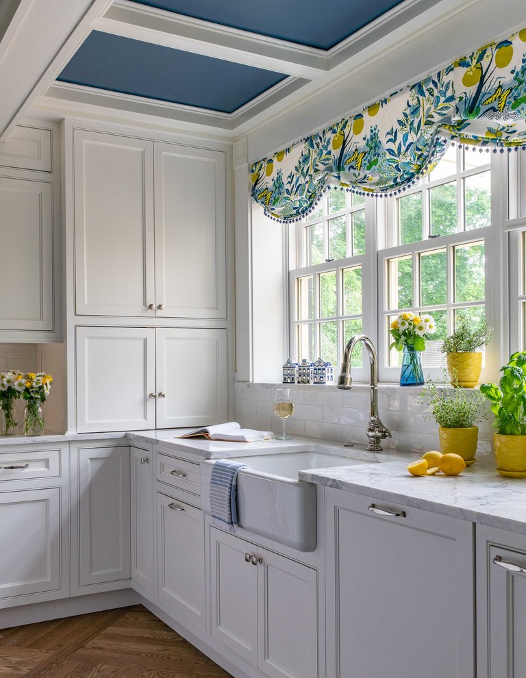 Inspiration for a traditional l-shaped kitchen in Boston with a farmhouse sink, beaded inset cabinets, white cabinets, white splashback, medium hardwood floors, brown floor and white benchtop.