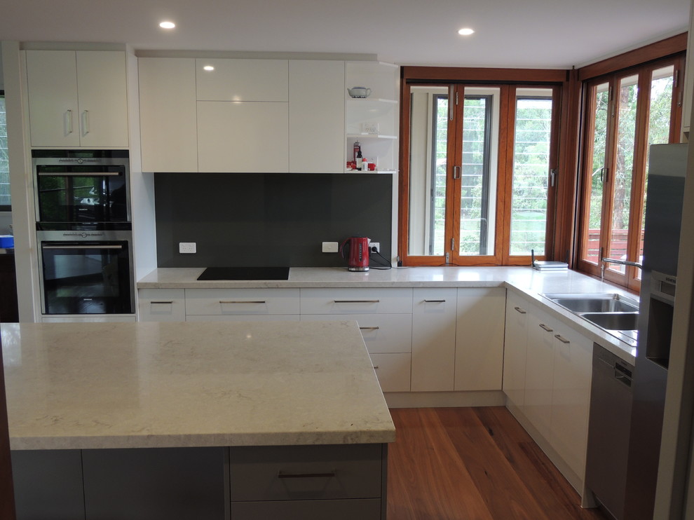 Design ideas for a large contemporary l-shaped eat-in kitchen in Brisbane with a drop-in sink, flat-panel cabinets, white cabinets, quartz benchtops, grey splashback, glass sheet splashback, stainless steel appliances, dark hardwood floors and with island.
