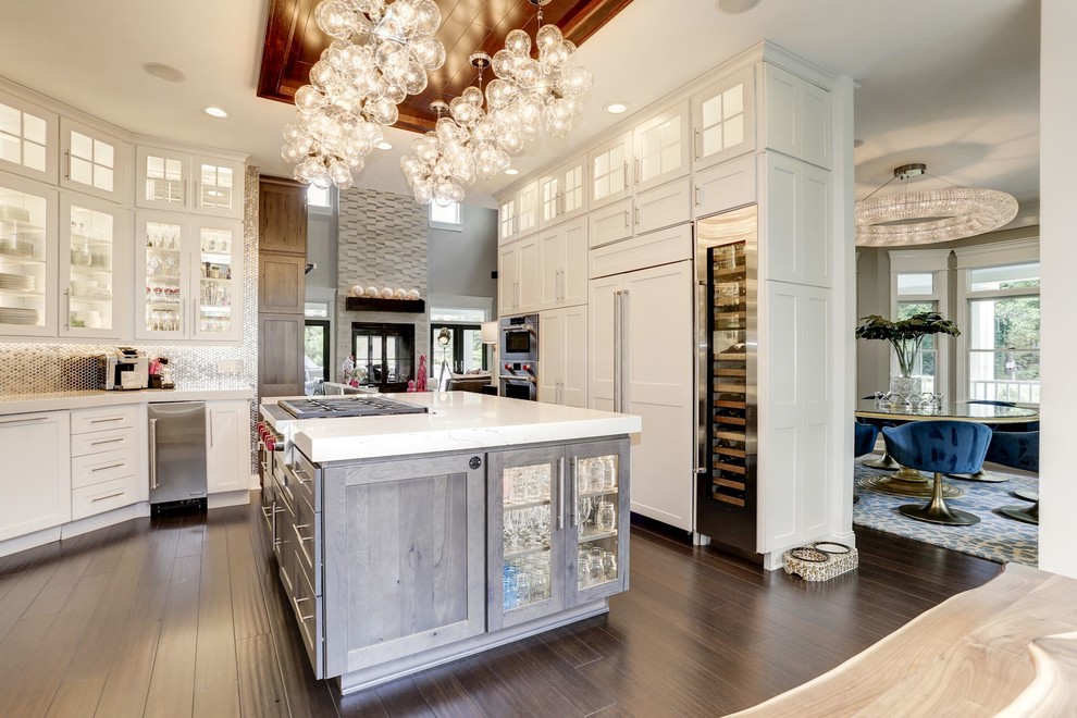 This is an example of a mid-sized transitional u-shaped eat-in kitchen in Baltimore with an undermount sink, glass-front cabinets, white cabinets, onyx benchtops, metallic splashback, metal splashback, stainless steel appliances, dark hardwood floors, with island, brown floor and white benchtop.
