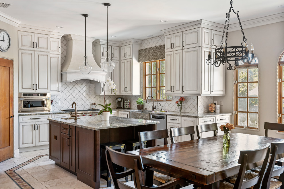 Inspiration for a large mediterranean u-shaped open plan kitchen in Tampa with a farmhouse sink, recessed-panel cabinets, beige cabinets, granite benchtops, white splashback, ceramic splashback, stainless steel appliances, ceramic floors, with island, beige floor and grey benchtop.