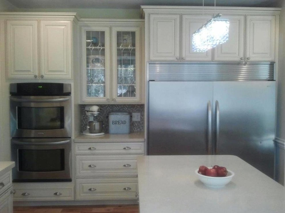 Kitchen - mid-sized medium tone wood floor kitchen idea with a farmhouse sink, raised-panel cabinets, white cabinets, solid surface countertops, multicolored backsplash, mosaic tile backsplash, stainless steel appliances and an island