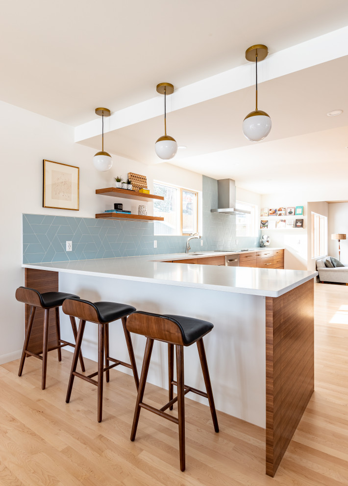 Design ideas for a large midcentury l-shaped eat-in kitchen in Calgary with a double-bowl sink, flat-panel cabinets, medium wood cabinets, quartz benchtops, blue splashback, subway tile splashback, stainless steel appliances, light hardwood floors, with island and white benchtop.