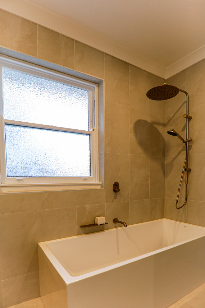 Photo of a medium sized classic ensuite half tiled bathroom in Sydney with raised-panel cabinets, medium wood cabinets, a built-in bath, a shower/bath combination, a two-piece toilet, beige tiles, cement tiles, beige walls, cement flooring, a vessel sink, wooden worktops, beige floors, a hinged door, brown worktops, double sinks, a freestanding vanity unit and a vaulted ceiling.