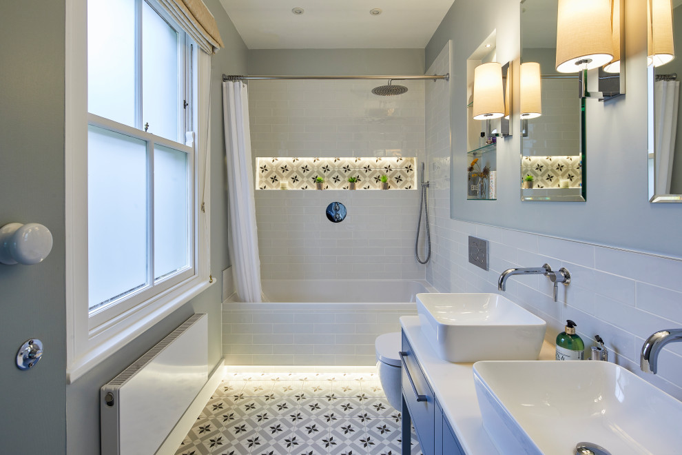 This is an example of a contemporary kids bathroom in Surrey with blue cabinets, a drop-in tub, a shower/bathtub combo, a wall-mount toilet, multi-coloured tile, ceramic tile, blue walls, porcelain floors, multi-coloured floor, a shower curtain, white benchtops and a double vanity.