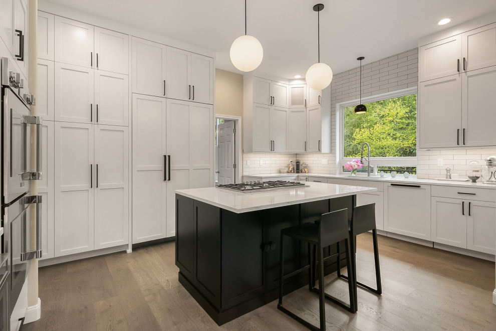 Inspiration for a large transitional u-shaped light wood floor enclosed kitchen remodel in Seattle with an undermount sink, shaker cabinets, white cabinets, quartz countertops, white backsplash, subway tile backsplash, an island, white countertops and paneled appliances