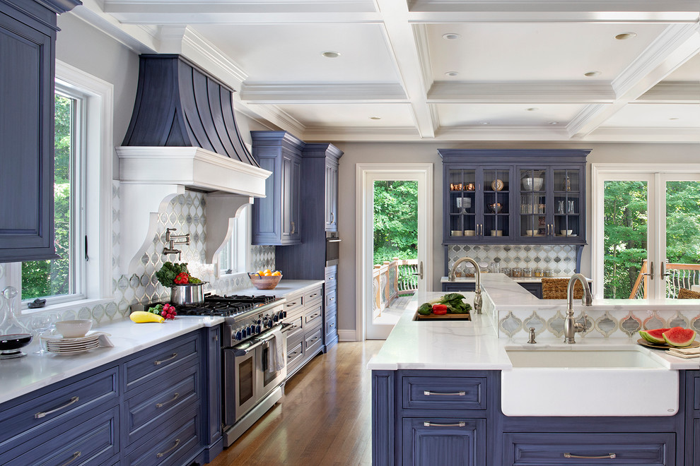 Design ideas for a mid-sized traditional kitchen in New York with a farmhouse sink, blue cabinets, quartz benchtops, stainless steel appliances, medium hardwood floors, brown floor, white benchtop, multi-coloured splashback, with island and recessed-panel cabinets.