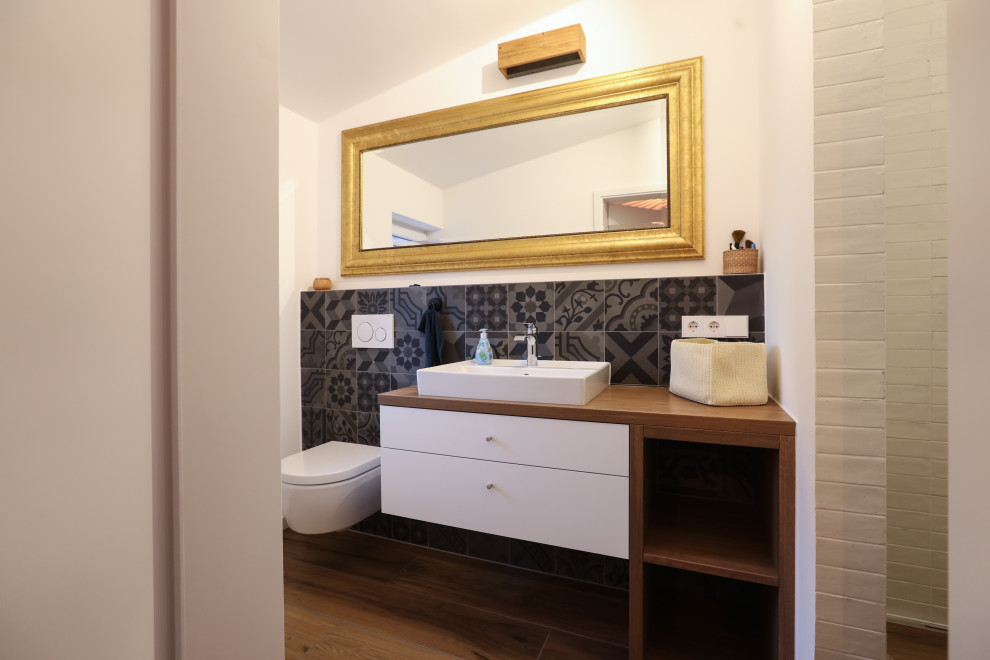 Inredning av ett skandinaviskt mellanstort brun brunt badrum med dusch, med släta luckor, vita skåp, en vägghängd toalettstol, grå kakel, keramikplattor, vita väggar, ett fristående handfat, brunt golv och med dusch som är öppen