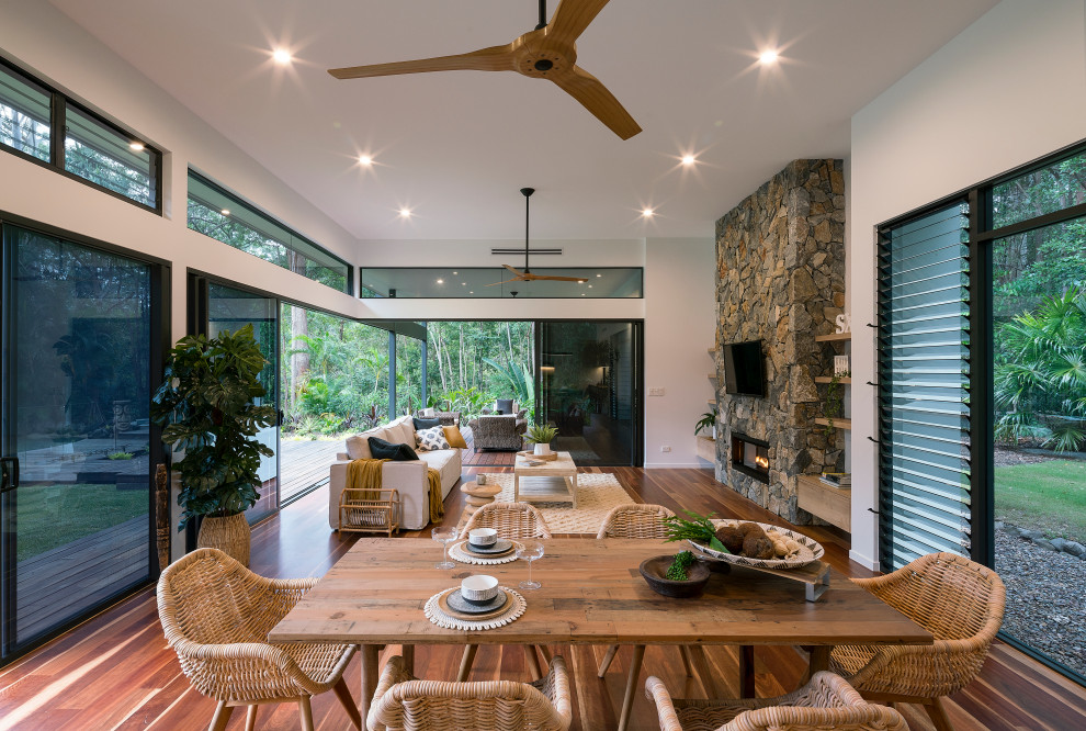 Photo of a contemporary open plan dining in Sunshine Coast with white walls, medium hardwood floors, a ribbon fireplace, a stone fireplace surround and brown floor.