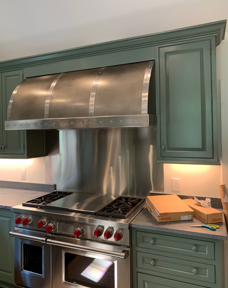Example of a transitional u-shaped kitchen design with a farmhouse sink, raised-panel cabinets, green cabinets, soapstone countertops, stainless steel appliances and an island