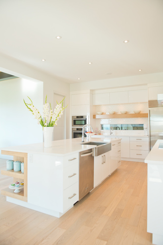 This is an example of a contemporary kitchen in Calgary with a farmhouse sink, flat-panel cabinets, white cabinets, white splashback, subway tile splashback and stainless steel appliances.