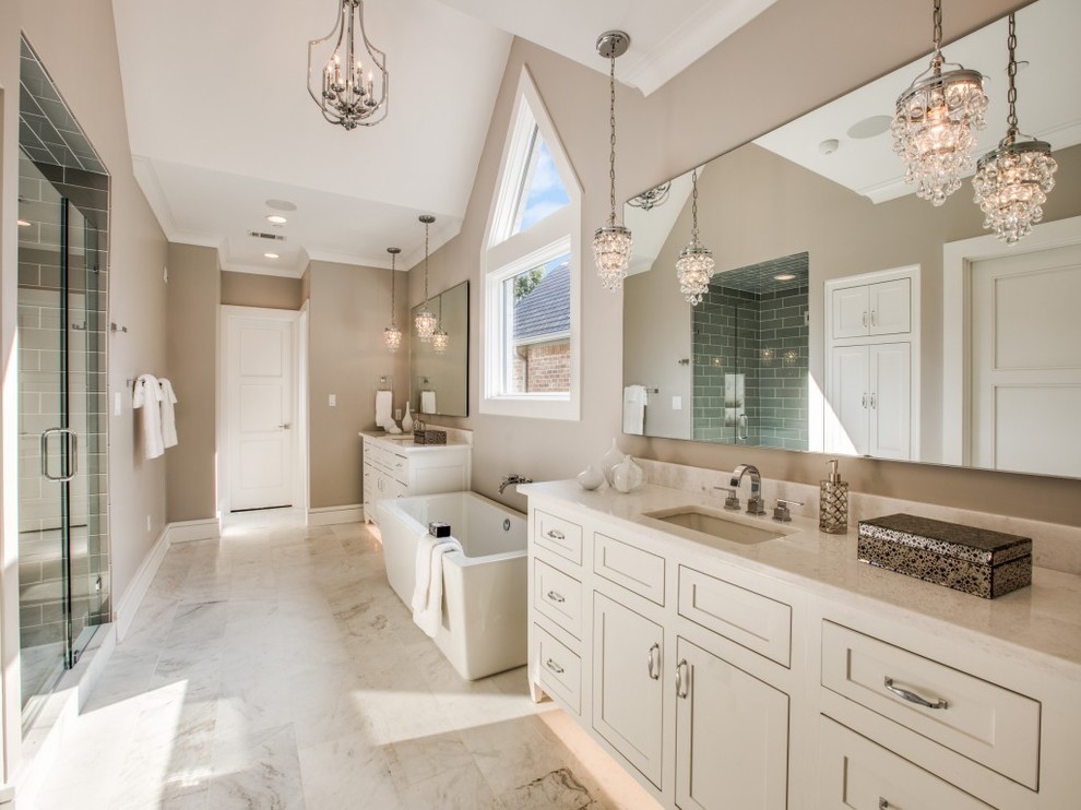 This is an example of a large transitional master bathroom in Dallas with shaker cabinets, white cabinets, a freestanding tub, a double shower, a one-piece toilet, beige tile, grey walls, marble floors, an undermount sink, marble benchtops, white floor, a hinged shower door and porcelain tile.