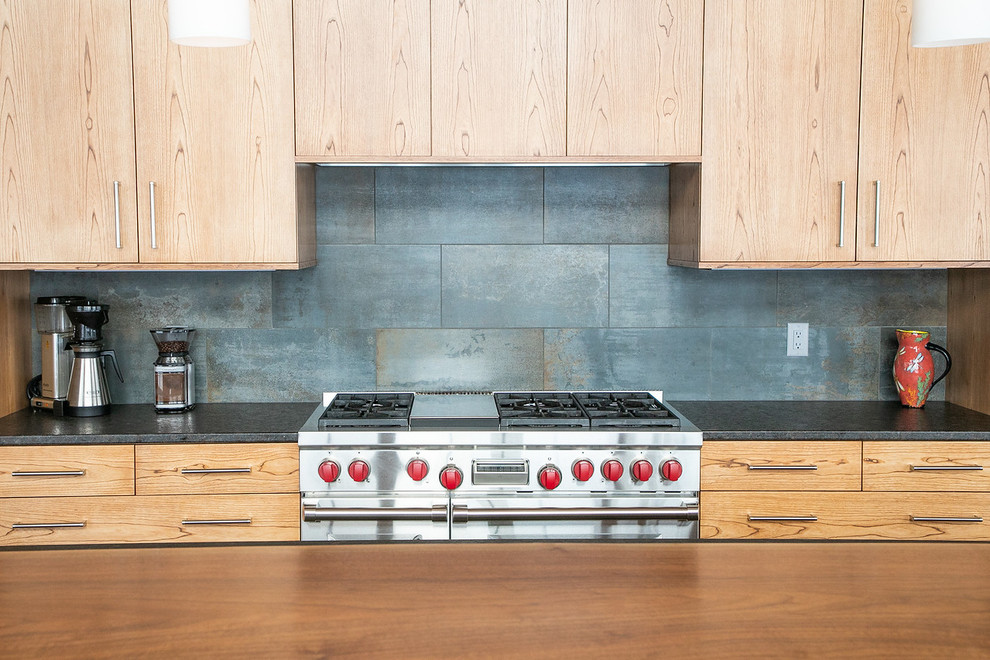 Large mountain style l-shaped medium tone wood floor and brown floor open concept kitchen photo with flat-panel cabinets, light wood cabinets, granite countertops, black backsplash, stainless steel appliances, an island, black countertops, a double-bowl sink and porcelain backsplash