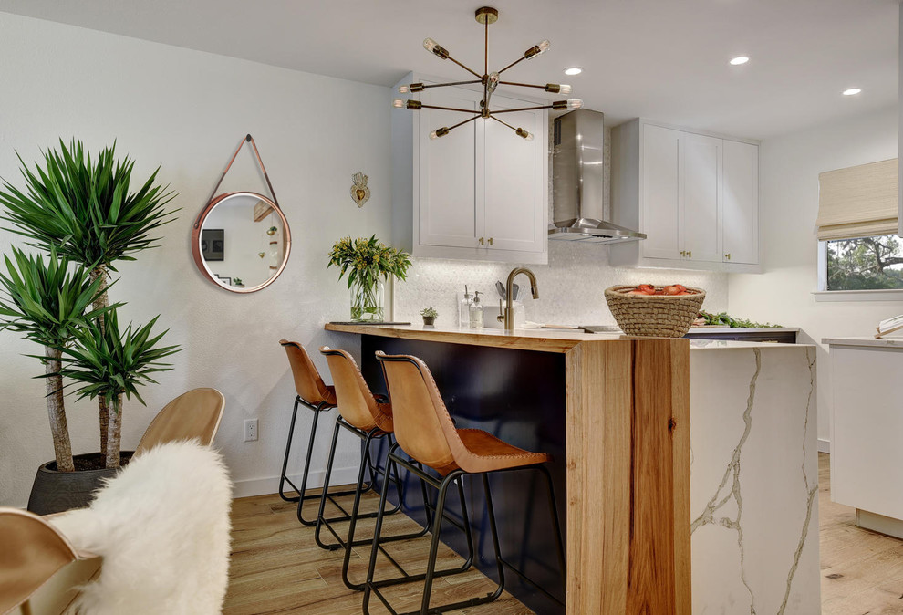 Design ideas for a mid-sized modern l-shaped eat-in kitchen in Austin with a farmhouse sink, shaker cabinets, white cabinets, quartz benchtops, white splashback, mosaic tile splashback, stainless steel appliances, light hardwood floors, a peninsula and beige floor.