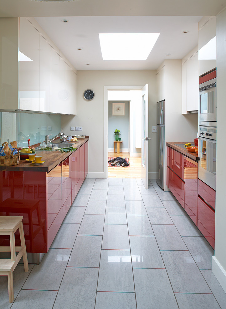Design ideas for a contemporary galley separate kitchen in Dublin with wood benchtops, red cabinets, flat-panel cabinets, glass sheet splashback and stainless steel appliances.