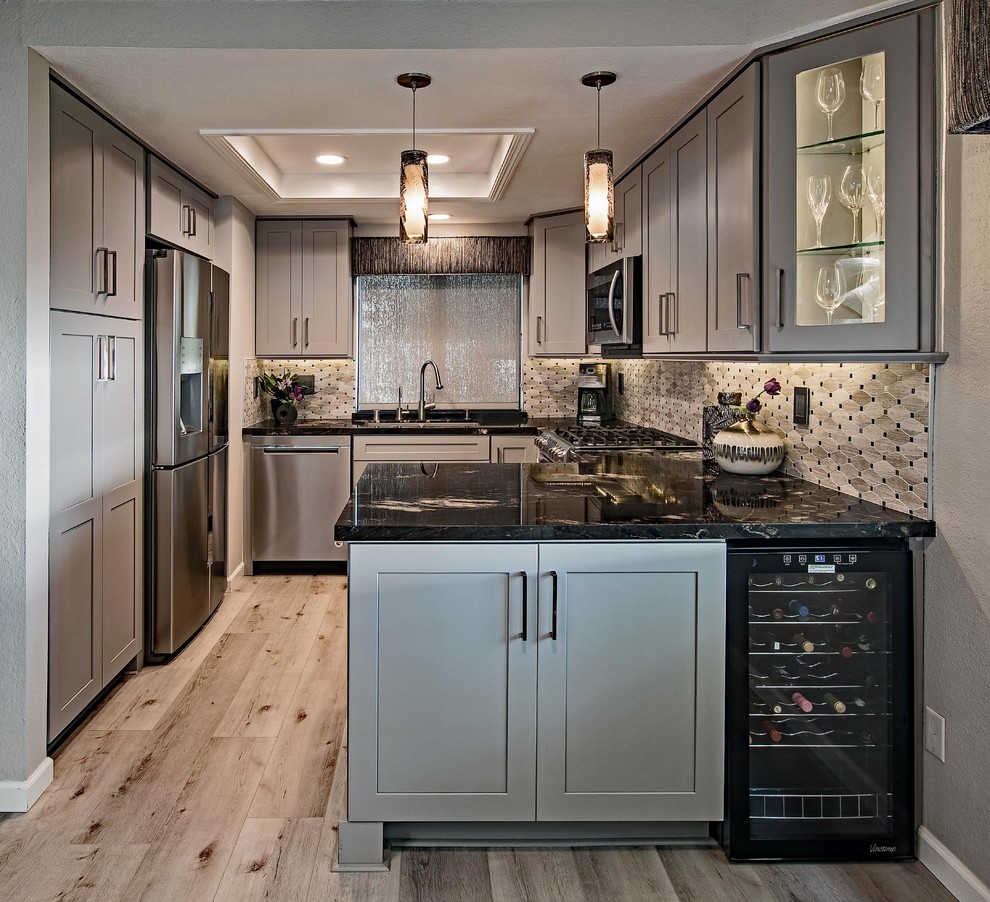 Design ideas for a transitional u-shaped kitchen in Orange County with an undermount sink, shaker cabinets, grey cabinets, beige splashback, mosaic tile splashback, stainless steel appliances, medium hardwood floors, a peninsula, brown floor and black benchtop.