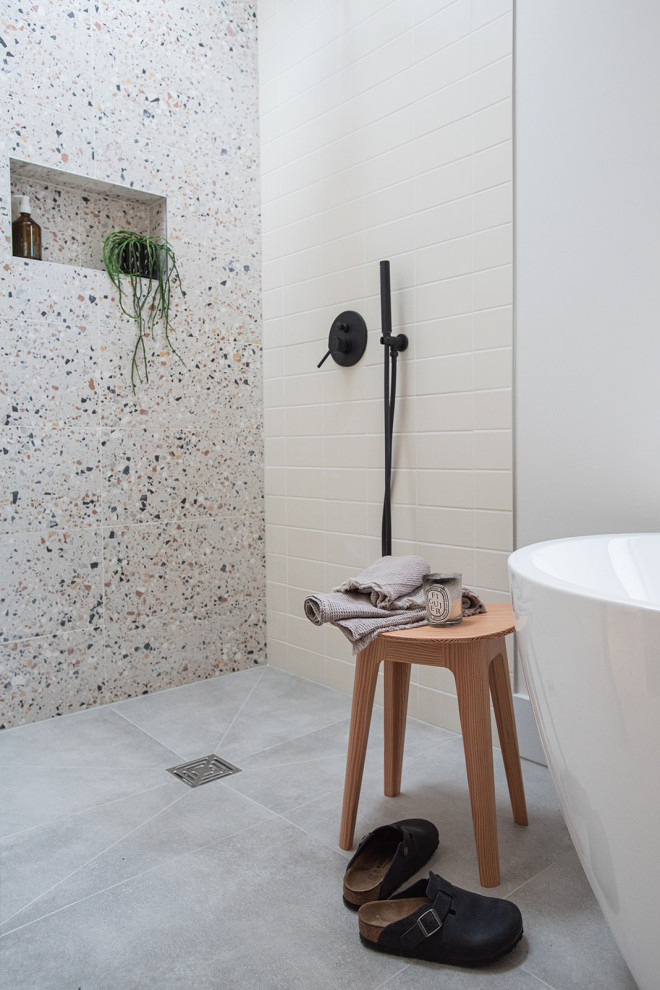 Bild på ett mellanstort funkis badrum för barn, med ett fristående badkar, en öppen dusch, en vägghängd toalettstol, beige kakel, porslinskakel, flerfärgade väggar, cementgolv, ett väggmonterat handfat, träbänkskiva, grått golv och med dusch som är öppen