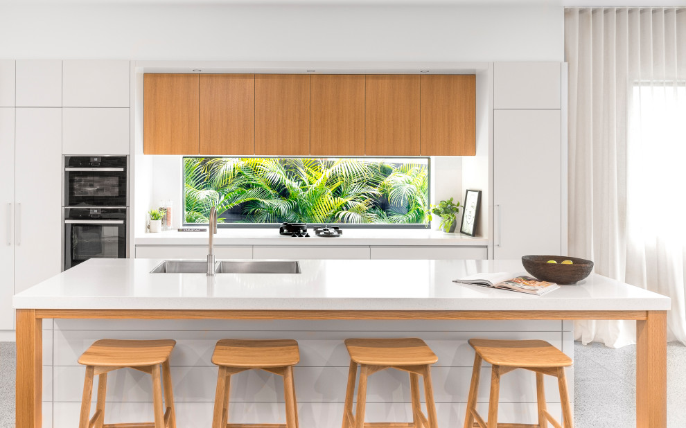 Inspiration for a mid-sized contemporary galley kitchen in Sydney with a double-bowl sink, flat-panel cabinets, white cabinets, quartz benchtops, white splashback, with island, white benchtop, window splashback, panelled appliances and grey floor.