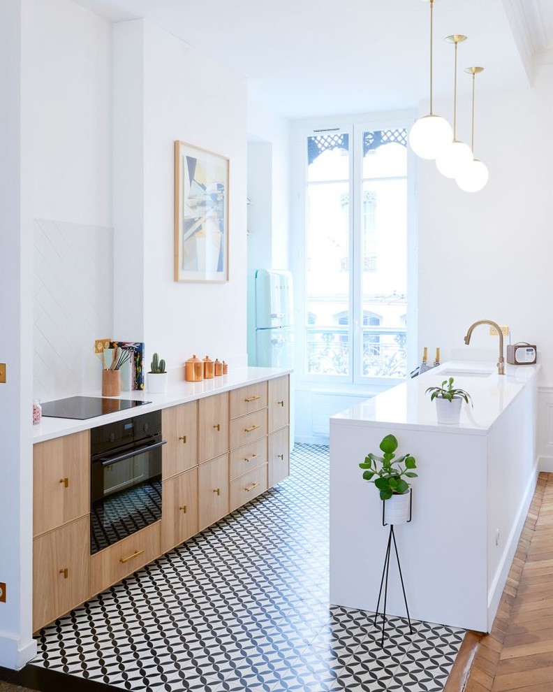 Design ideas for a mid-sized contemporary galley open plan kitchen in Lyon with an integrated sink, light wood cabinets, white splashback, black appliances, cement tiles, with island and multi-coloured floor.