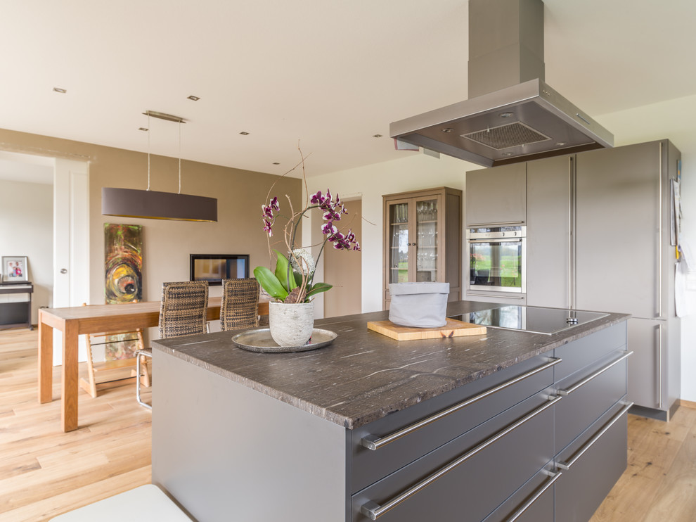 Design ideas for a large contemporary galley eat-in kitchen in Other with flat-panel cabinets, grey cabinets, granite benchtops, stainless steel appliances, medium hardwood floors, with island, an undermount sink, white splashback, limestone splashback, brown floor and brown benchtop.