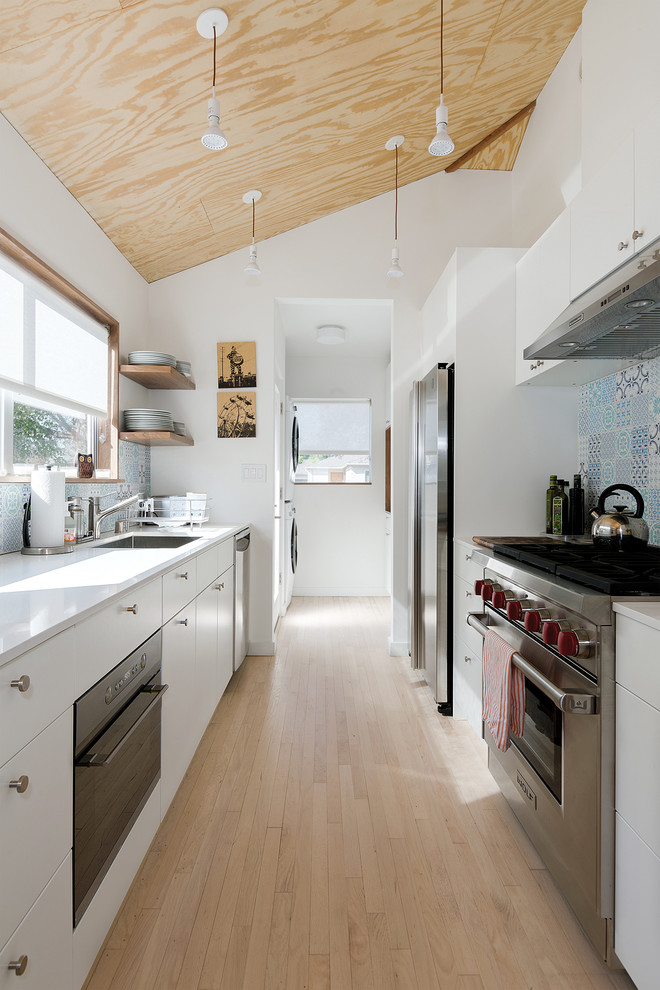 Photo of a mid-sized scandinavian galley separate kitchen in Los Angeles with a single-bowl sink, flat-panel cabinets, white cabinets, quartz benchtops, blue splashback, porcelain splashback, stainless steel appliances and light hardwood floors.