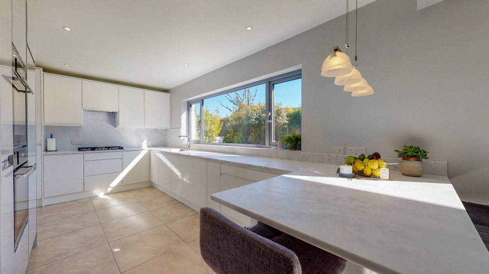 This is an example of a mid-sized modern u-shaped kitchen in Other with an integrated sink, glass-front cabinets, white cabinets, solid surface benchtops, white splashback, panelled appliances, porcelain floors, a peninsula, beige floor and white benchtop.