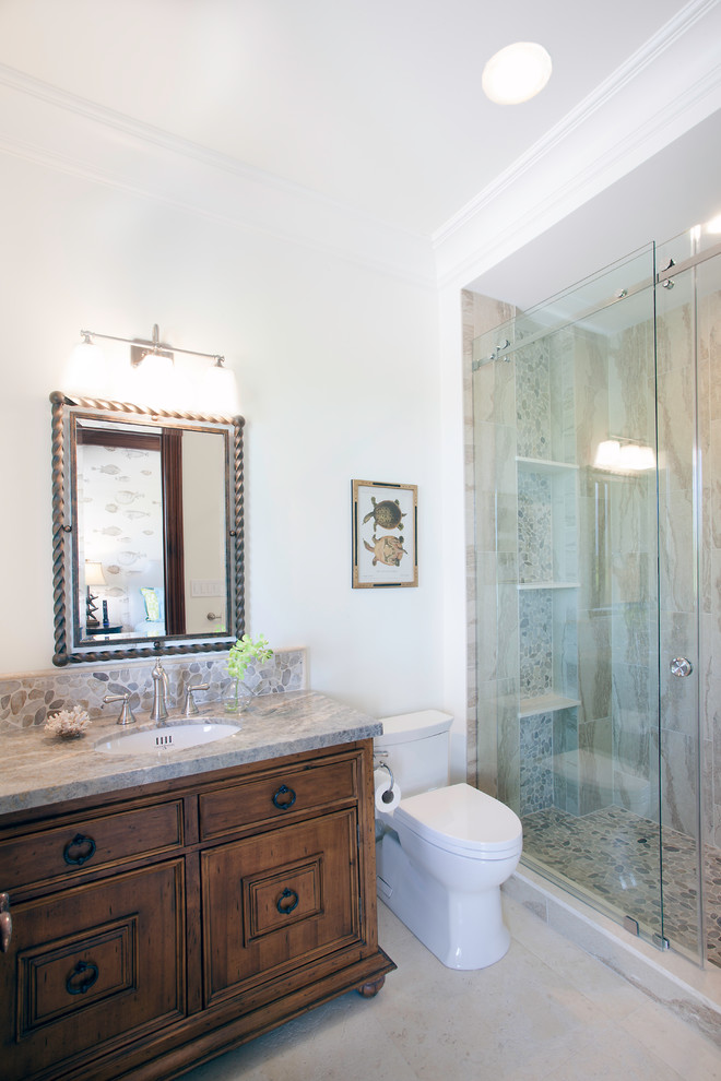 Inspiration for an expansive tropical 3/4 bathroom in Miami with furniture-like cabinets, brown cabinets, beige tile, white walls, an alcove shower, a two-piece toilet, marble, porcelain floors, a drop-in sink, granite benchtops, beige floor and a sliding shower screen.