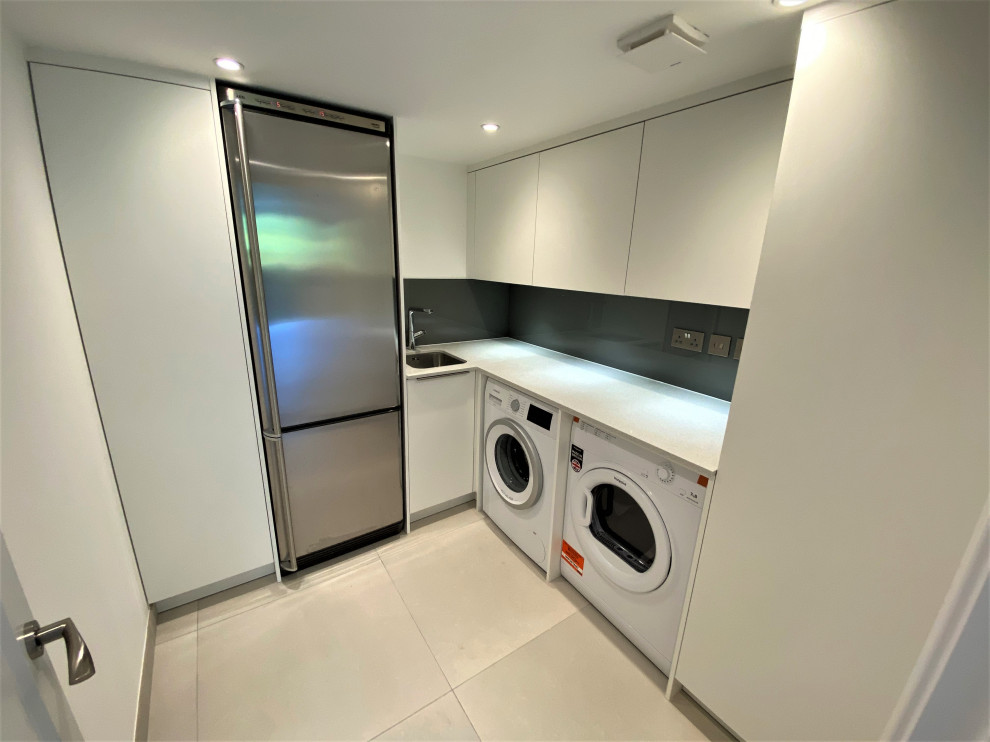 Inspiration for a small l-shaped utility room in London with flat-panel cabinets, white cabinets, quartzite benchtops, brown splashback, glass sheet splashback, white walls, a side-by-side washer and dryer and white benchtop.